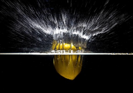 A fresh yellow lemon (Citrus limonum) falls into the water, creating a splash and air bubbles,