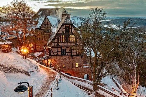 Timbered house in evening lighting, surrounded by snow-covered paths and trees at dusk, The Hotel
