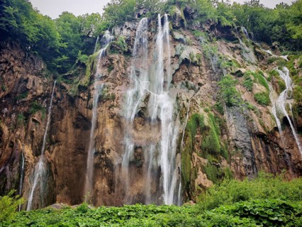 High waterfalls fall impressively over rocky cliffs and disappear into the dense forest, Plitvice