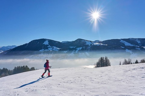 Sportive senior woman hiking with snow shoes in the snowy Allgaeu Alps above Lake Alosee,