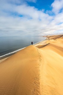 Young woman standing on a sand dune in front of impressive desert landscape and sea Atlantic coast