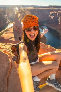 Young woman smiling while taking a selfie on the edge of horseshoe bend canyon, enjoying travel,