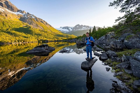 Young man standing on a stone on the lakeside, enjoying the landscape, picturesque mountain scenery