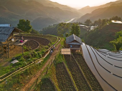 Aerial view of woman with pink backpack sitting on a wooden house at sunset in the mountains and