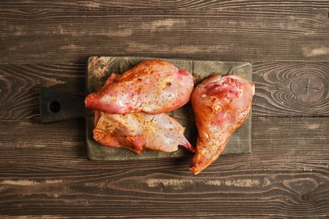 Top view of marinated rabbit meat on a wooden cutting board. They show signs of seasoning. The