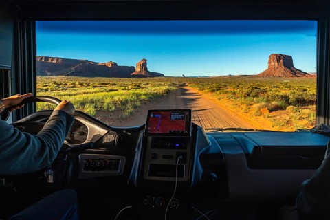 Person driving a recreational vehicle on a dirt road, experiencing a desert road trip through