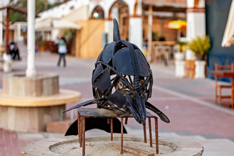 Ornate metal dolphin sculpture in a sunny urban passage, statue on the beach promenade of Paracas