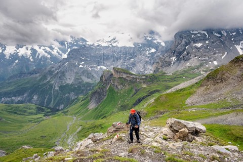 Mountaineers on a hiking trail, view of a green high valley and steep mountain peaks, cloudy