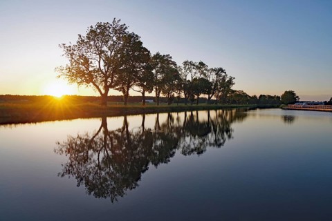 Sunset over a series of trees reflecting in water, Hajstorp, Göta Canal, Västra Götalands län,