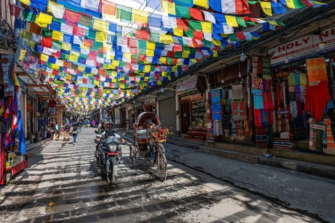 Bicycle rickshaw in a sparsely busy street with prayer flags and souvenir shops, Thamel, Kathmandu,