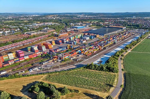 Aerial view of a large container terminal with freight trains, shipping containers, cranes, and