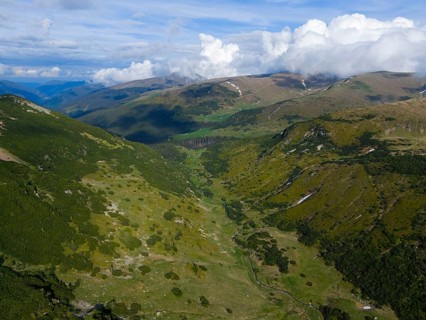 Extensive green mountain landscape with valleys under a dramatic cloudy sky, aerial view, near