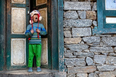 Little Nepalese boy from the Sherpa ethnic group yawning in front of a front door, Solu Khumbu
