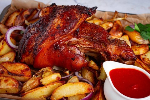Baked pork knuckle, with potato slices, on a tray, with red sauce, homemade, no people, light