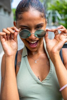 Young woman with tattoos and piercings joyfully gazing over her round sunglasses, expressing