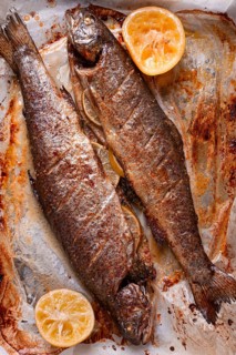 Two fish are being cooked on a baking sheet in a home kitchen. Lemon slices are placed beside the