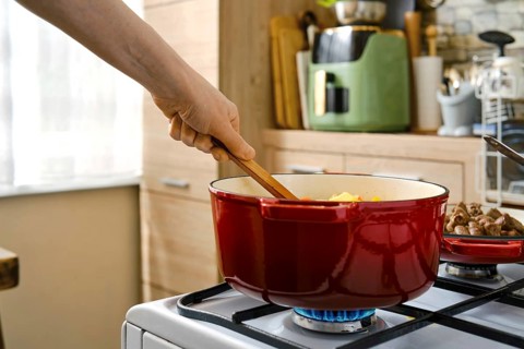 A person stirs a pot on a stove in a kitchen. The pot contains vegetables and is on a gas burner.