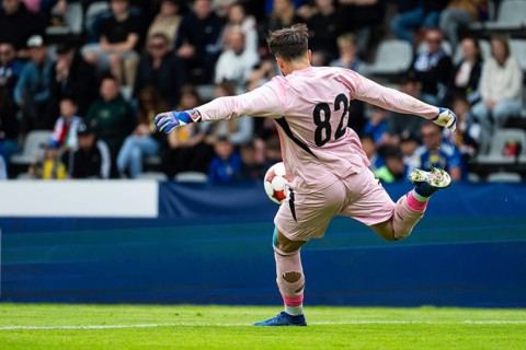 Goalkeeper in pink kit kicking the ball during a football match in a crowded stadium, dynamic