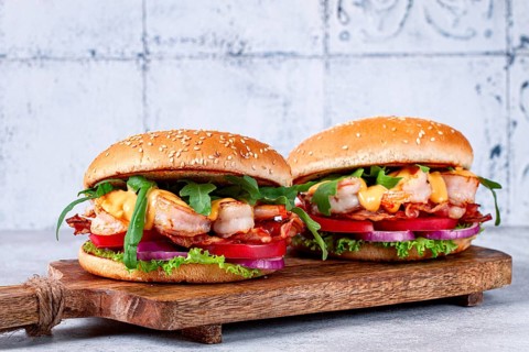 Two shrimp burgers and buns with sesame seeds, bacon, lettuce, tomatoes and onions, On a wooden