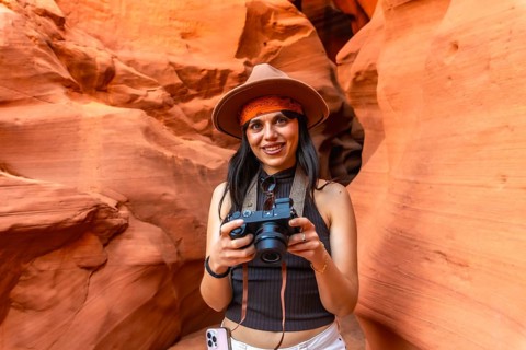 Woman traveler in hat and bandana smiling and holding a camera while photographing the sculpted red