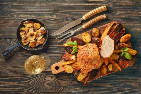 Dinner scene shows roasted pork fillet served on wooden board with various vegetables. Side dish