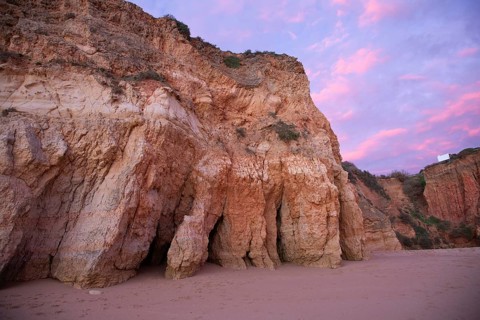 Steep cliffs on the beach under a pink sky during sunset, sandstone cliffs on Praia de tres Irmaos