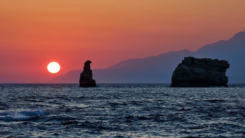 Red sunset over the sea with rocks in the foreground and mountains in the background, sunset, South