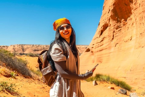 Young woman smiling and holding a mobile phone, experiencing a solo desert adventure while