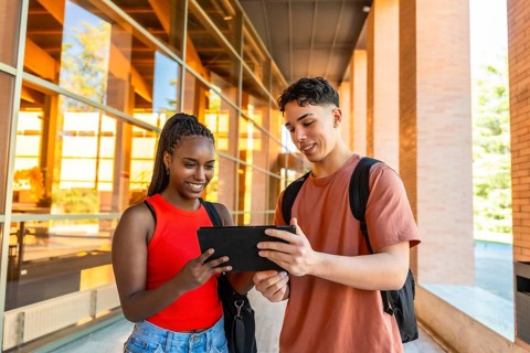 Diverse students standing outdoors on university campus, smiling and collaborating while looking at