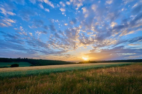 A silent sunset over a wide field with dramatic cloud formations interspersed with orange light,