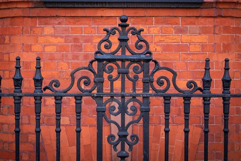 Black, ornate wrought iron fence in front of a brown-red brick wall, Chelsea, London, England,