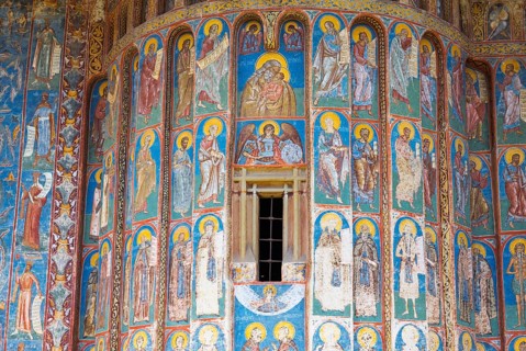 Wall with frescoes of figures of saints and windows, mostly in shades of blue and gold, exterior