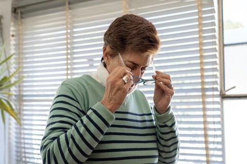 Close-up portrait of an older woman bringing blue reading glasses to her face with both hands,