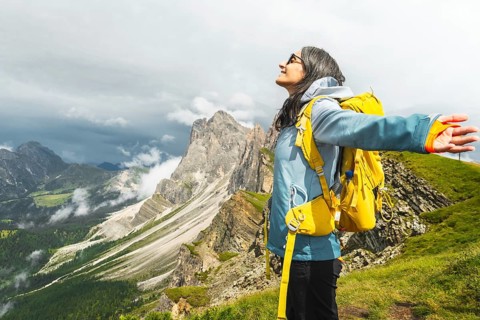 Happy female traveler yellow backpack standing outstretched arms mountain ridge line Seceda South