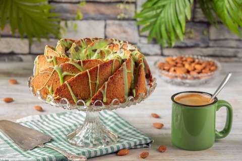 A cake with green icing next to a cup of coffee and almonds