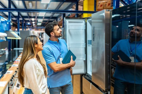 Sales assistant holding a tablet and explaining features of a stainless steel refrigerator to a