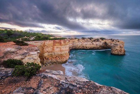 Stormy sunrise scene at Praia de Albandeira beach in Algarve, Portugal, with Arco de Albandeira,