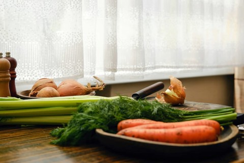 Unpeeled onion on a cutting board. Fresh celery, carrots and fresh dill on a kitchen table. Light