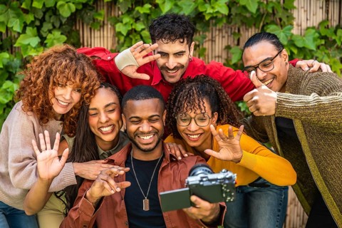 Diverse group of smiling friends creating social media content together with a camera, sharing