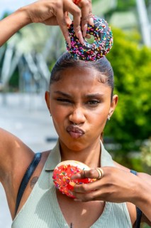 Young woman with a playful expression balancing chocolate and strawberry iced donuts with colorful