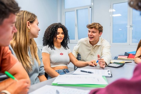 Group of diverse university students collaborating and discussing academic work at a table in a