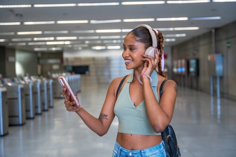 Young woman with headphones and a backpack standing in a subway station, smiling while listening to