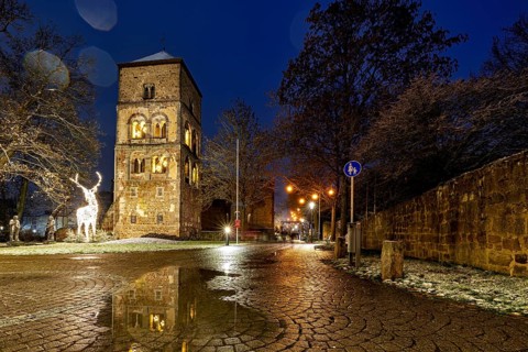A stone tower illuminated at dusk, surrounded by cobblestones and sculptures, The tower of the