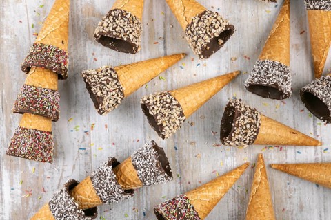 Ice cream cones with colorful sprinkles, chocolate and nuts on wooden background