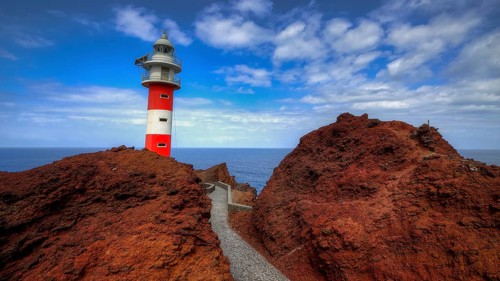 Punta de Teno, lighthouse on rocky cliffs with rocky path, blue sky and sea in the background,