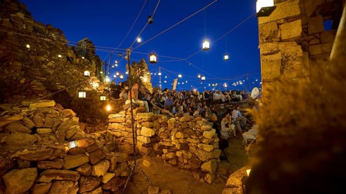 Open-air cinema, people gathered in a rocky area at night under twinkling lights, Kastro, old