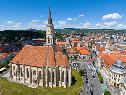 Neo-Gothic church with red tile roof and high tower, surrounded by urban infrastructure, aerial