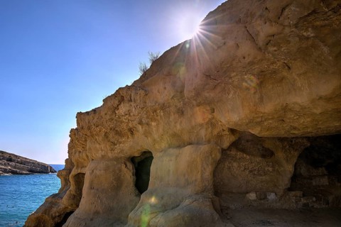 Neolithic caves, former hippie paradise, rocky coastal cave with light beam over the sea and blue