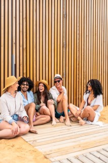 Group of diverse friends in summer clothes laughing and relaxing on a wooden boardwalk at the