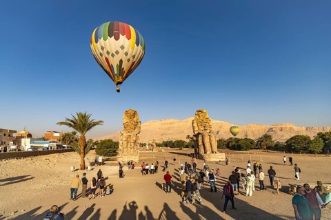 Travel groups and hot air balloon at the Colossi of Memnon in the Nile Valley in West Thebes near